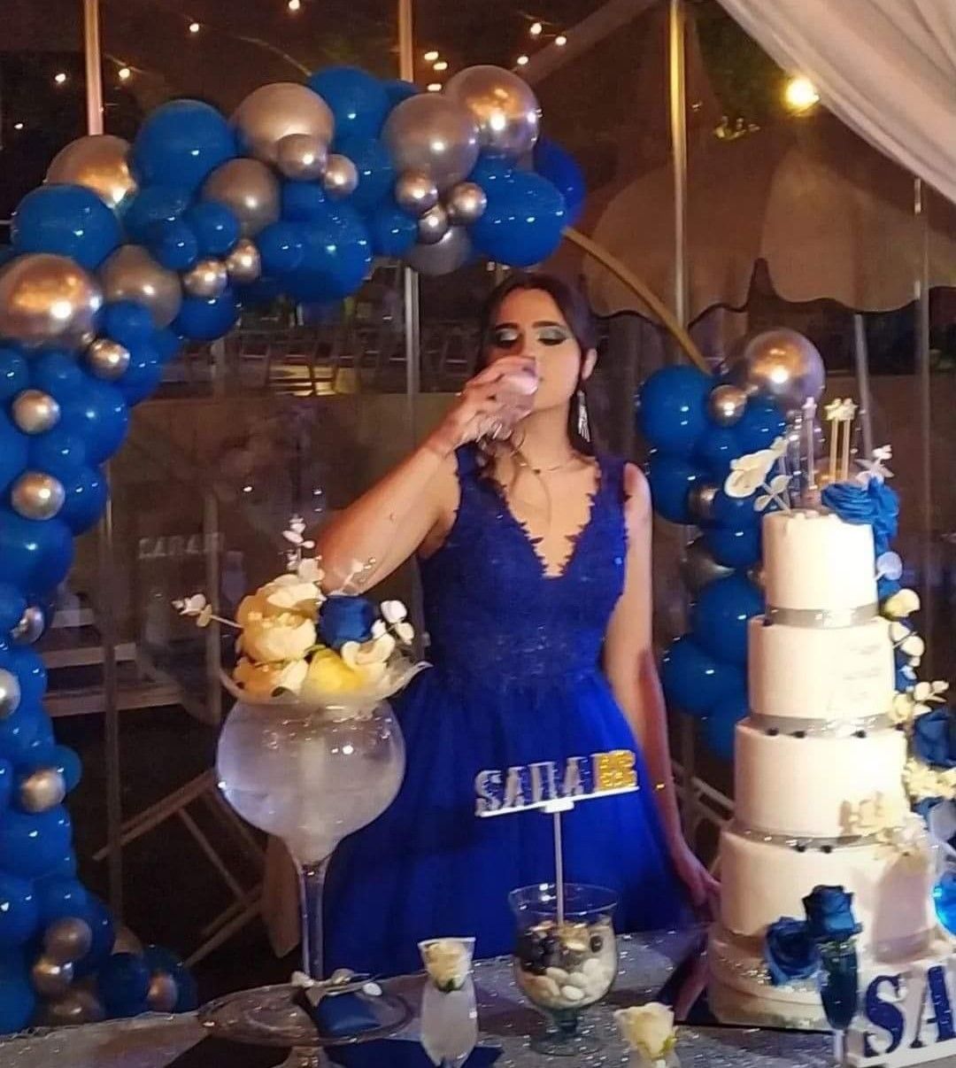 Una donna in abito blu beve da un bicchiere davanti a una torta