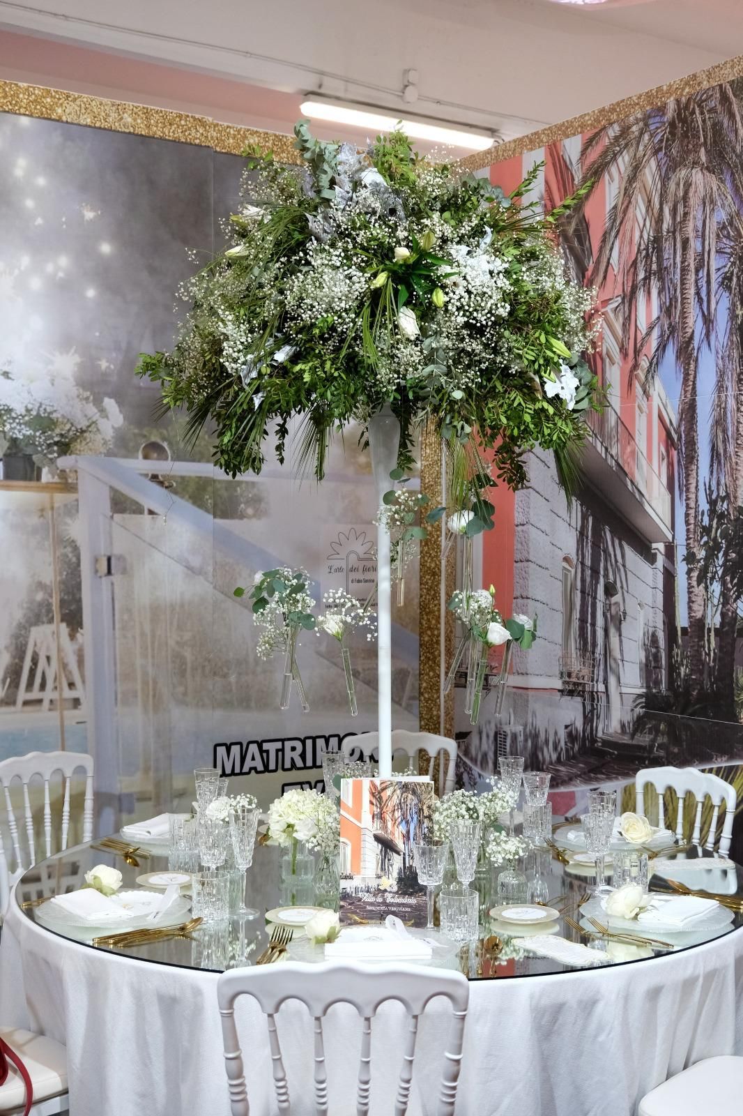 Un tavolo apparecchiato per un ricevimento di nozze con un vaso alto pieno di fiori.