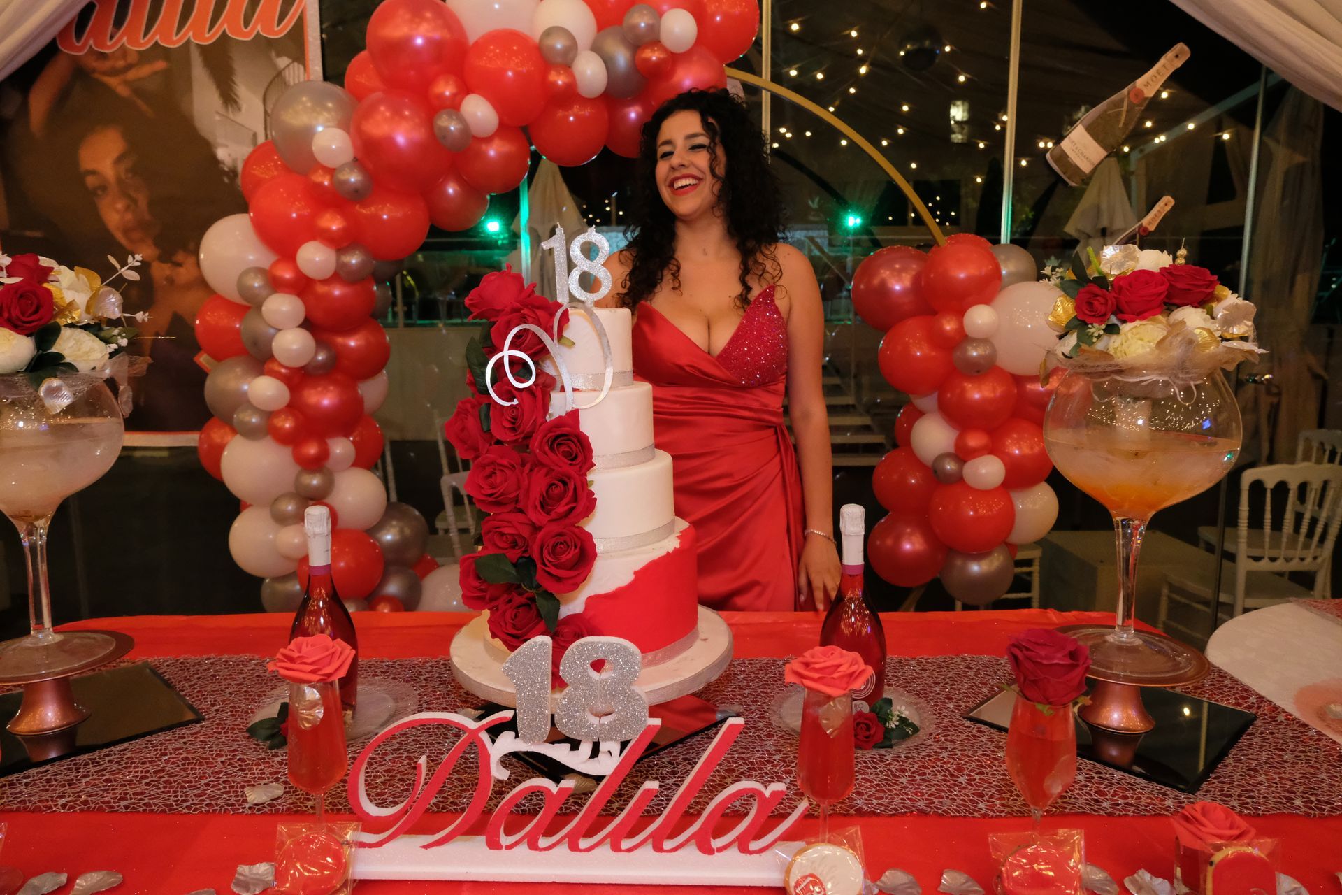 Una donna con un vestito rosso è in piedi davanti a una torta di compleanno.