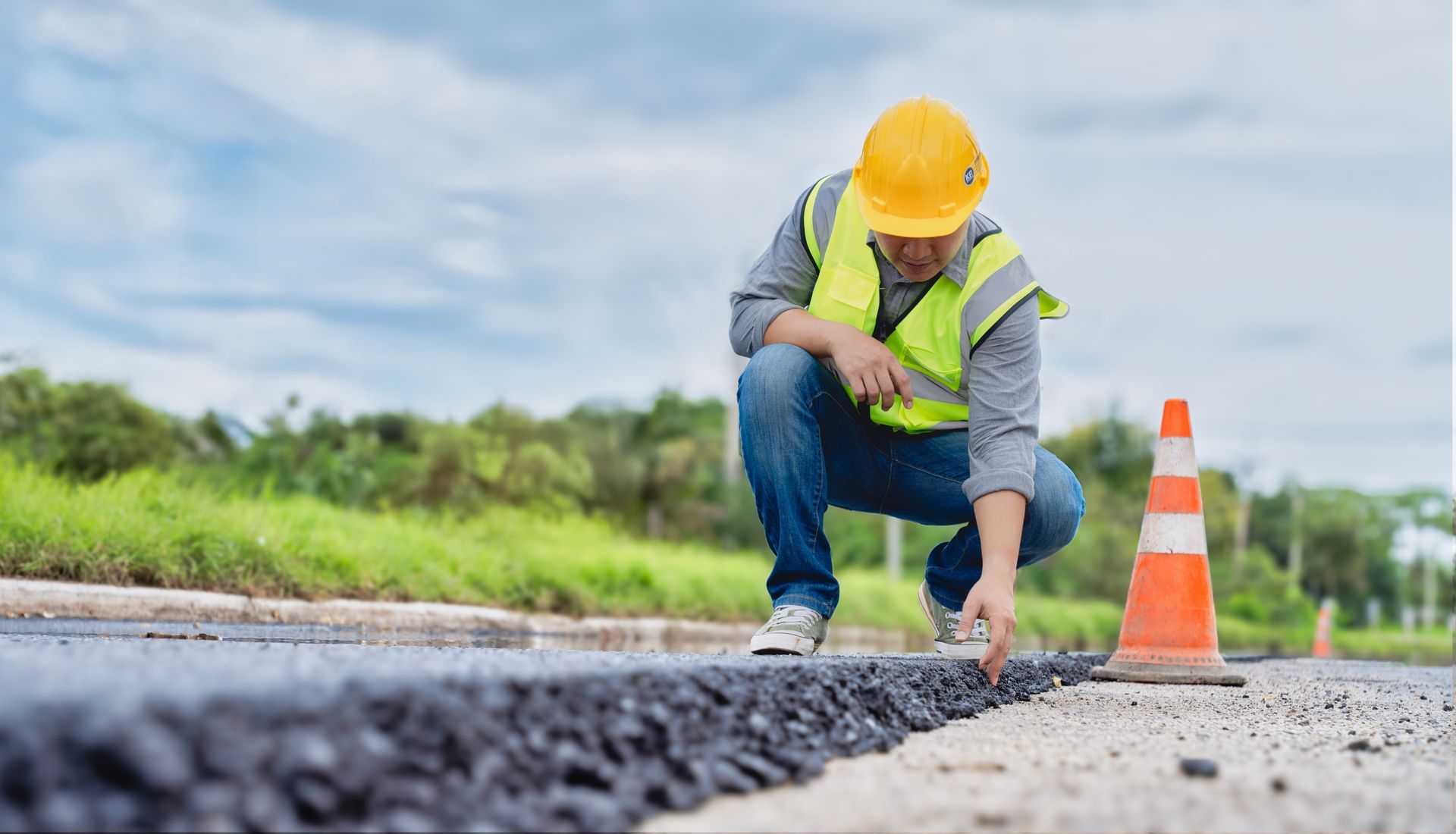 A male contractor checks a layer of asphalt on the ground while crouching. A male contractor checks a layer of asphalt on the ground while crouching.