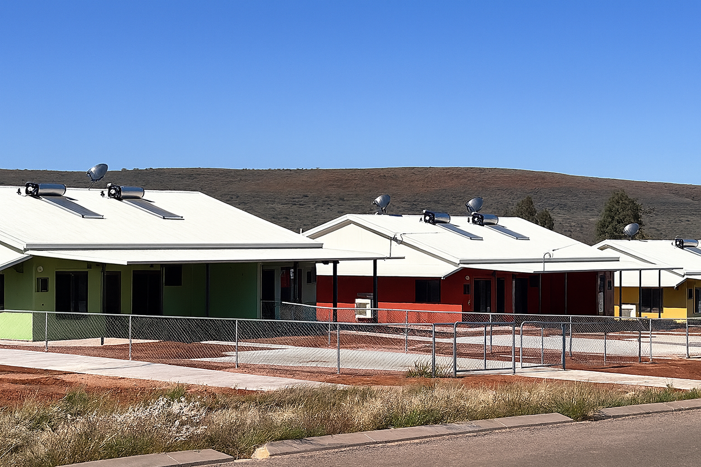 Row of colorful houses with white roofs and solar panels under a clear blue sky.