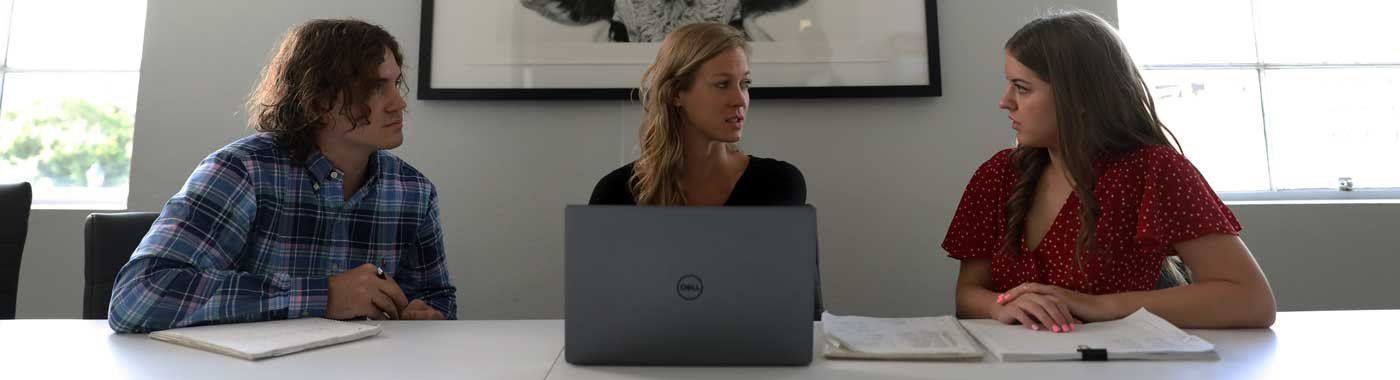 A group of people are sitting at a table with a laptop.