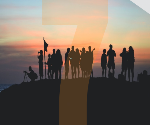 A group of people are standing on top of a hill at sunset.