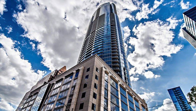 Looking up at a tall building with a blue sky and clouds in the background.