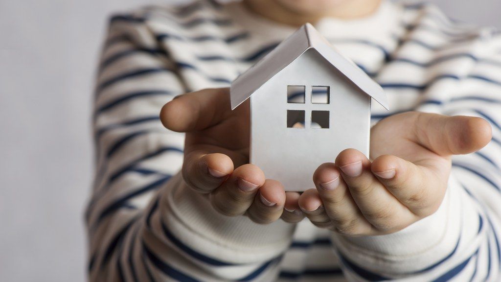 A person is holding a small paper house in their hands.