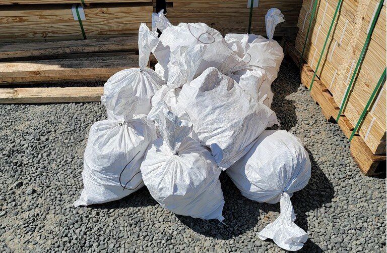 A pile of white stake bags sitting on top of gravel next to a wooden pallet.