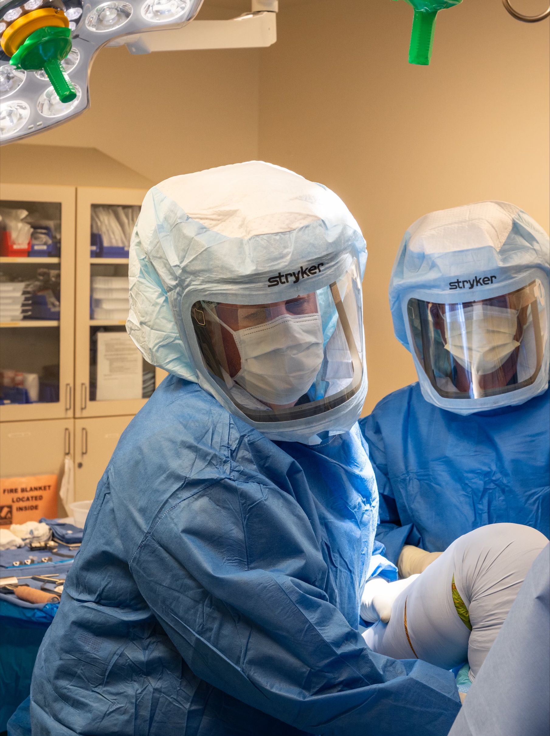 Two surgeons in blue scrubs, masks, and protective hoods operate in a sterile operating room.
