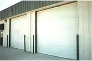Two large, white industrial garage doors on a building exterior with black support posts.