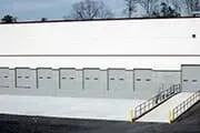 Loading dock with multiple bays, gray concrete, and a ramp. White and gray building exterior.
