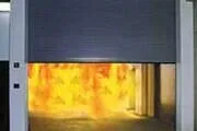 Fire behind a lowered gray fire shutter, with bright orange flames visible.