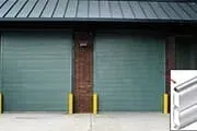 Green rolling garage doors in a building, with yellow bumpers and a close-up of a metal edge.