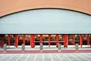 Building entrance with partially open, gray overhead door; red pillars visible behind.