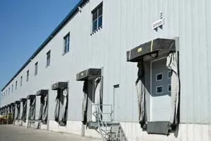 Loading docks on a warehouse with gray metal siding and black dock shelters under a blue sky.