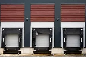 Three loading dock doors with brown roll-up shutters, white frames, and black bumpers.