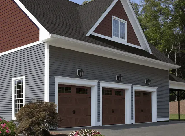 Three-bay garage with brown doors, gray siding, and a gabled roof with a maroon accent.