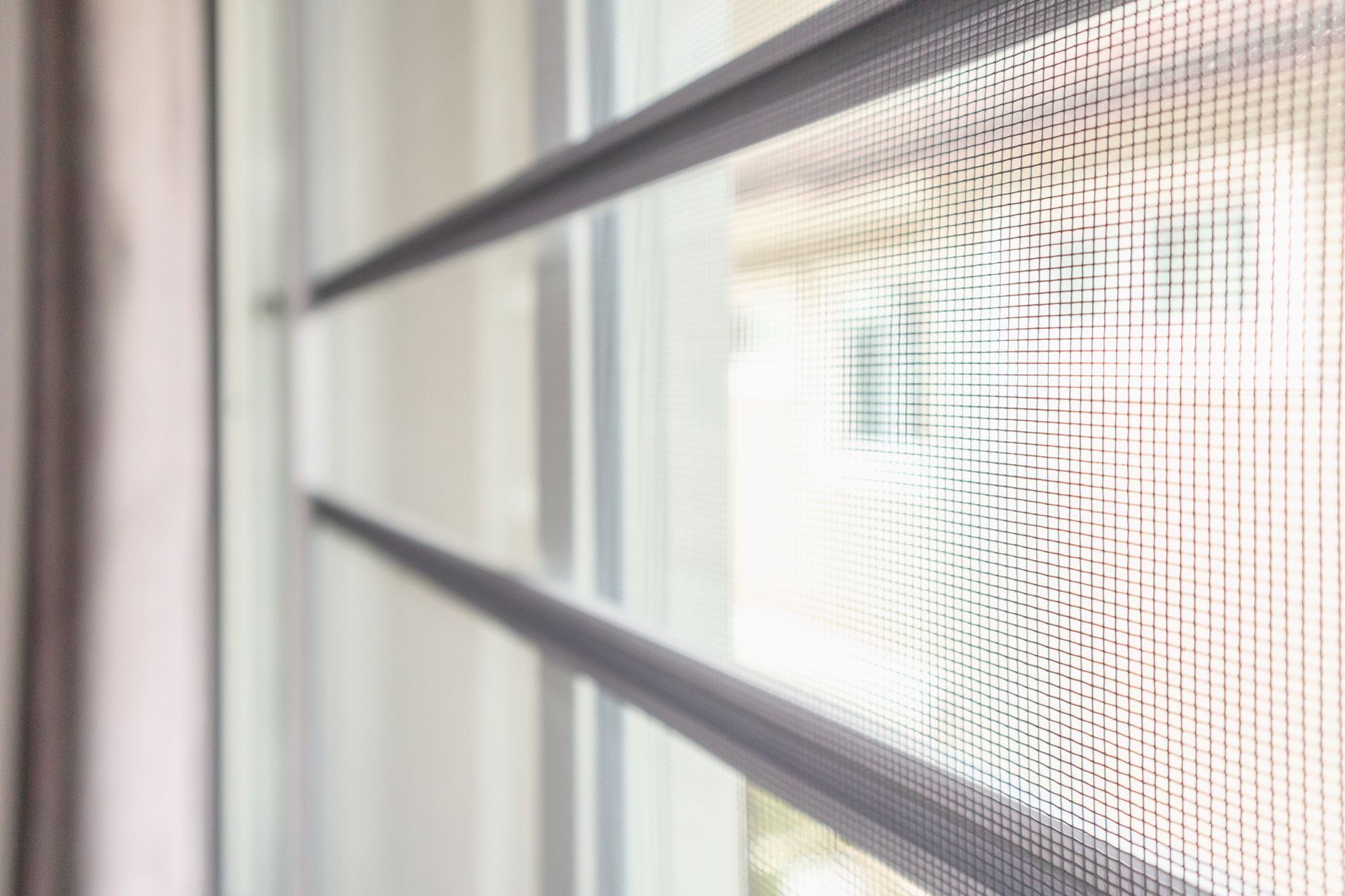 Close-up of a window screen with a gray frame and mesh, with a blurred view of the exterior visible through the window. Close-up of a window screen with a gray frame and mesh, with a blurred view of the exterior visible through the window.