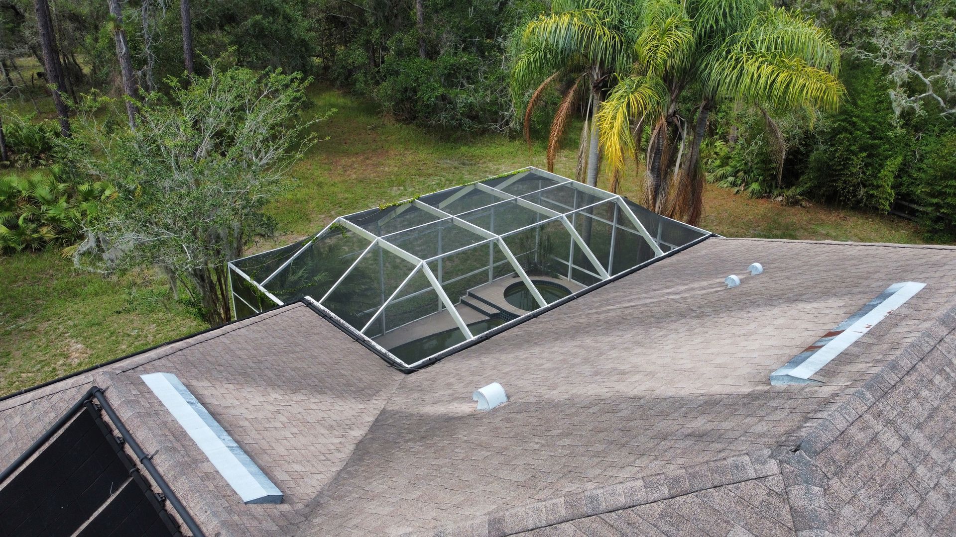 An aerial view of a residential roof featuring a large, rectangular glass skylight and a small, solar pool heater panel. An aerial view of a residential roof featuring a large, rectangular glass skylight and a small, solar pool heater panel.