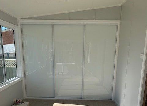 A Bedroom With White Sliding Glass Doors And A Window — Nambucca Glass in Nambucca Heads, NSW