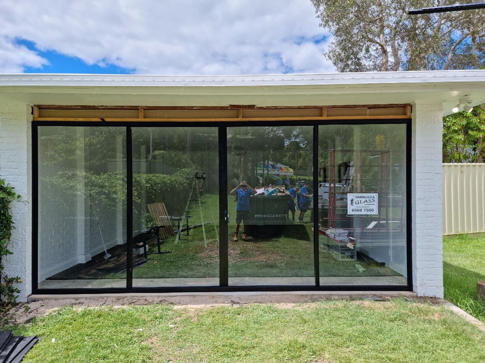 A White Brick Building With Large Glass Doors Reflecting A Backyard Scene