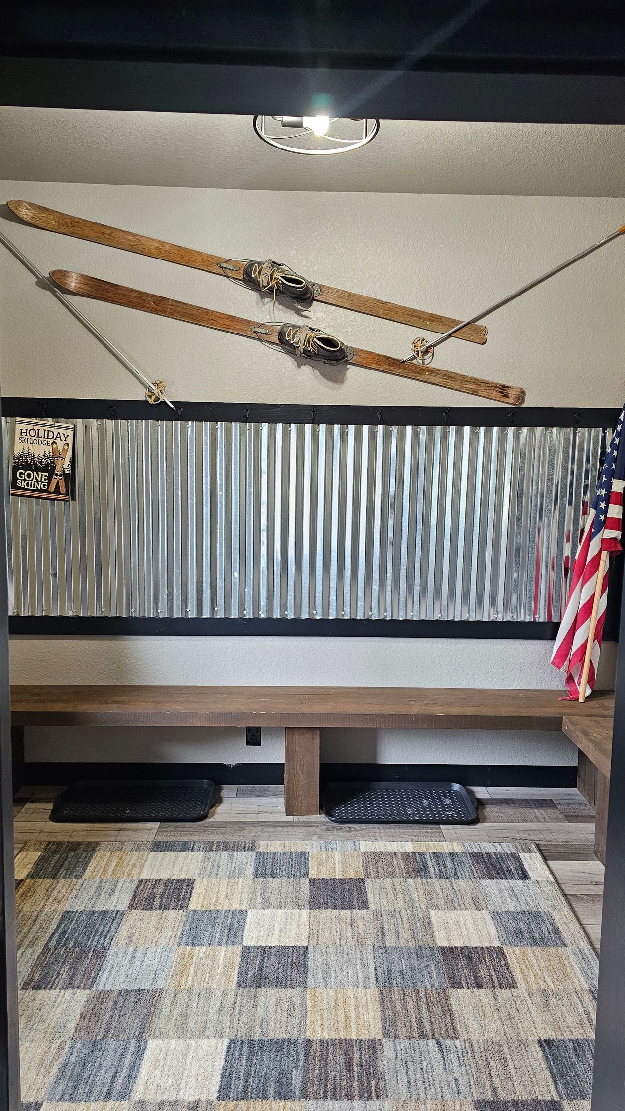 Rustic entryway with wooden bench, corrugated metal wall, and skis. An American flag hangs on the right.