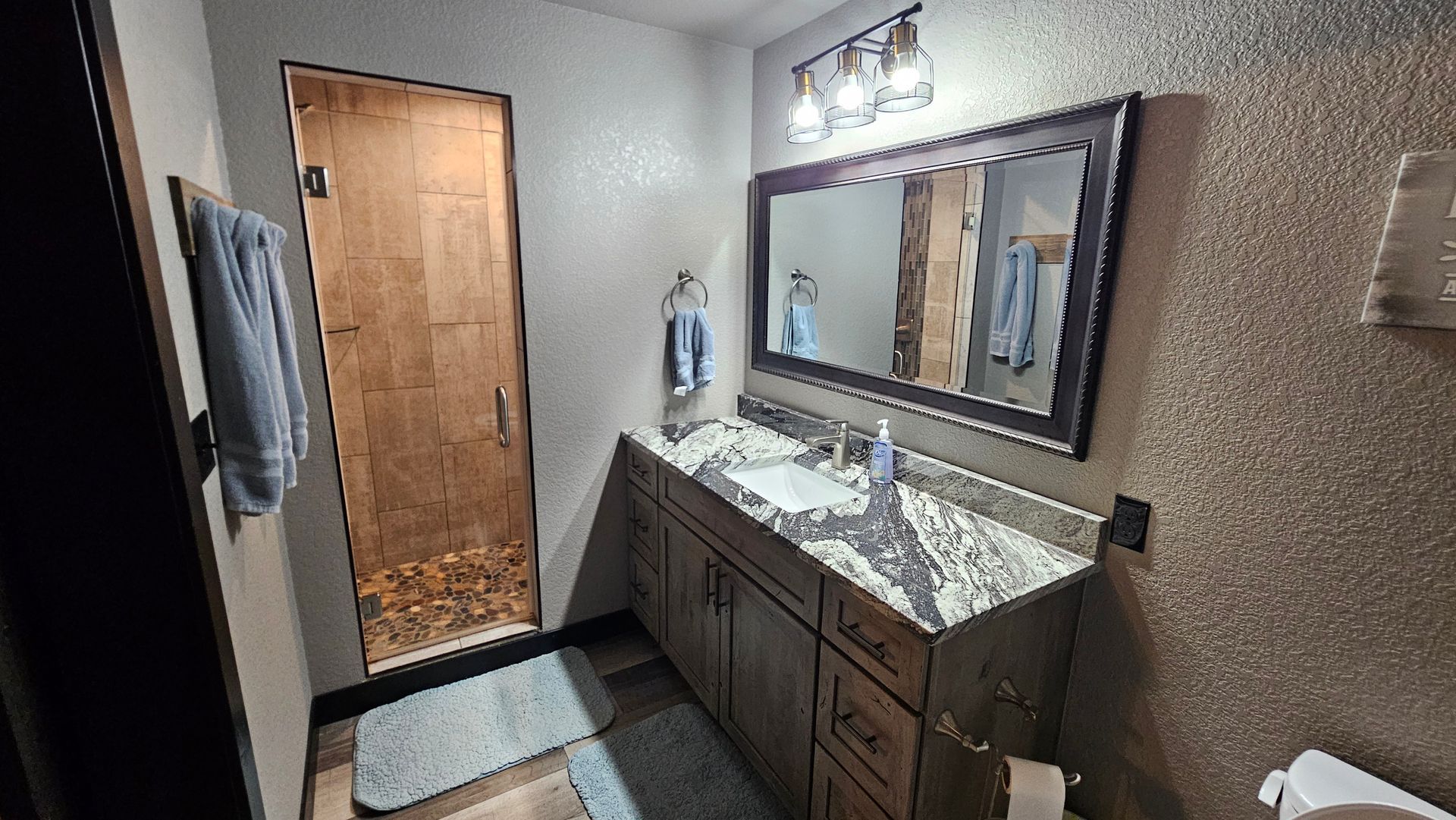 Bathroom with shower, vanity, and mirror. Brown shower door, dark wood vanity with granite countertop, and textured walls.