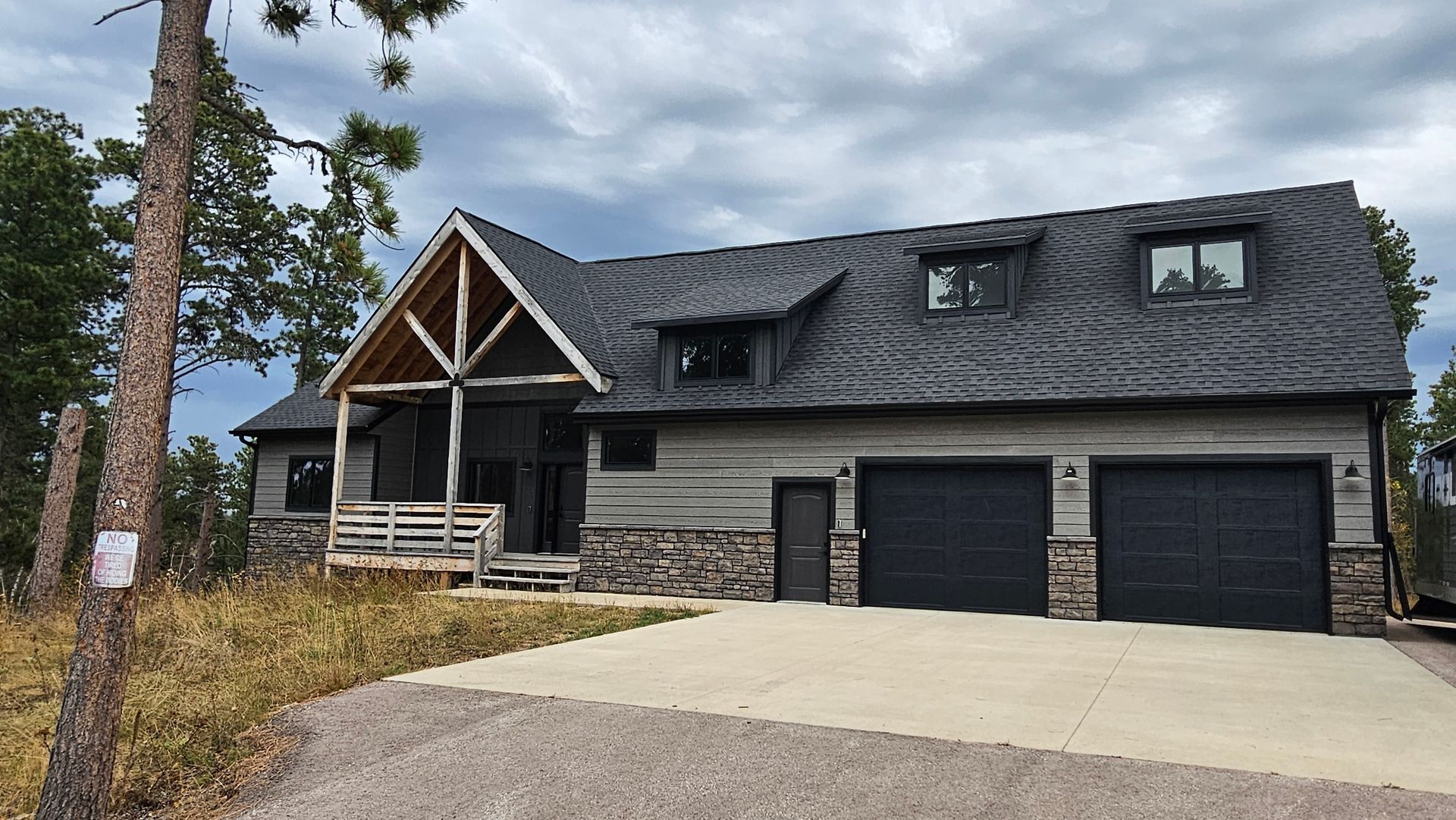 Gray house with porch, garage, and stone accents under a cloudy sky.