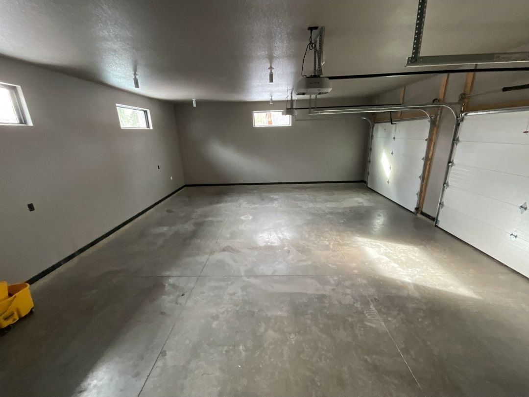 Empty garage with gray walls, cement floor, and two white garage doors.