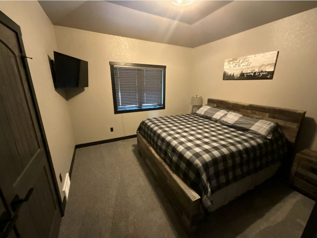Bedroom with a bed covered in a black and white checkered comforter, small TV on wall, and a window with closed blinds.