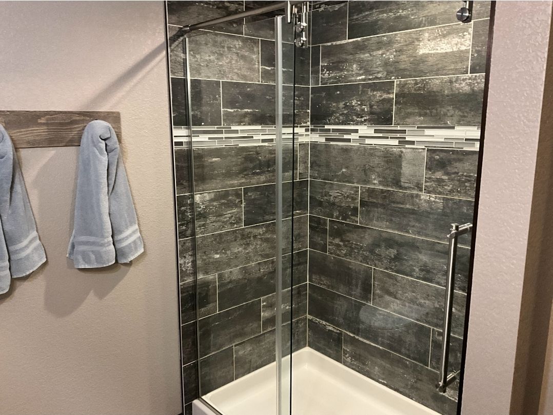 Shower stall with dark tile, glass door, and light gray towels.