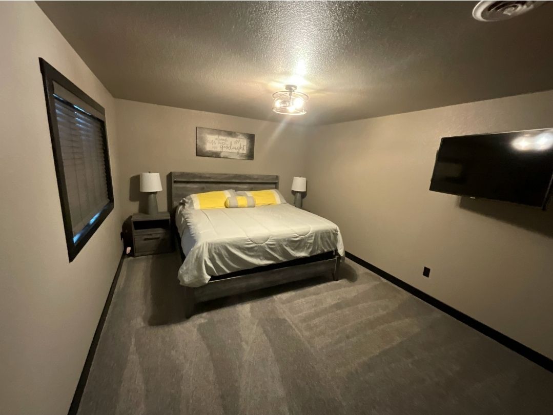 Bedroom with a gray bed, walls, and carpet; a TV mounted on the wall.