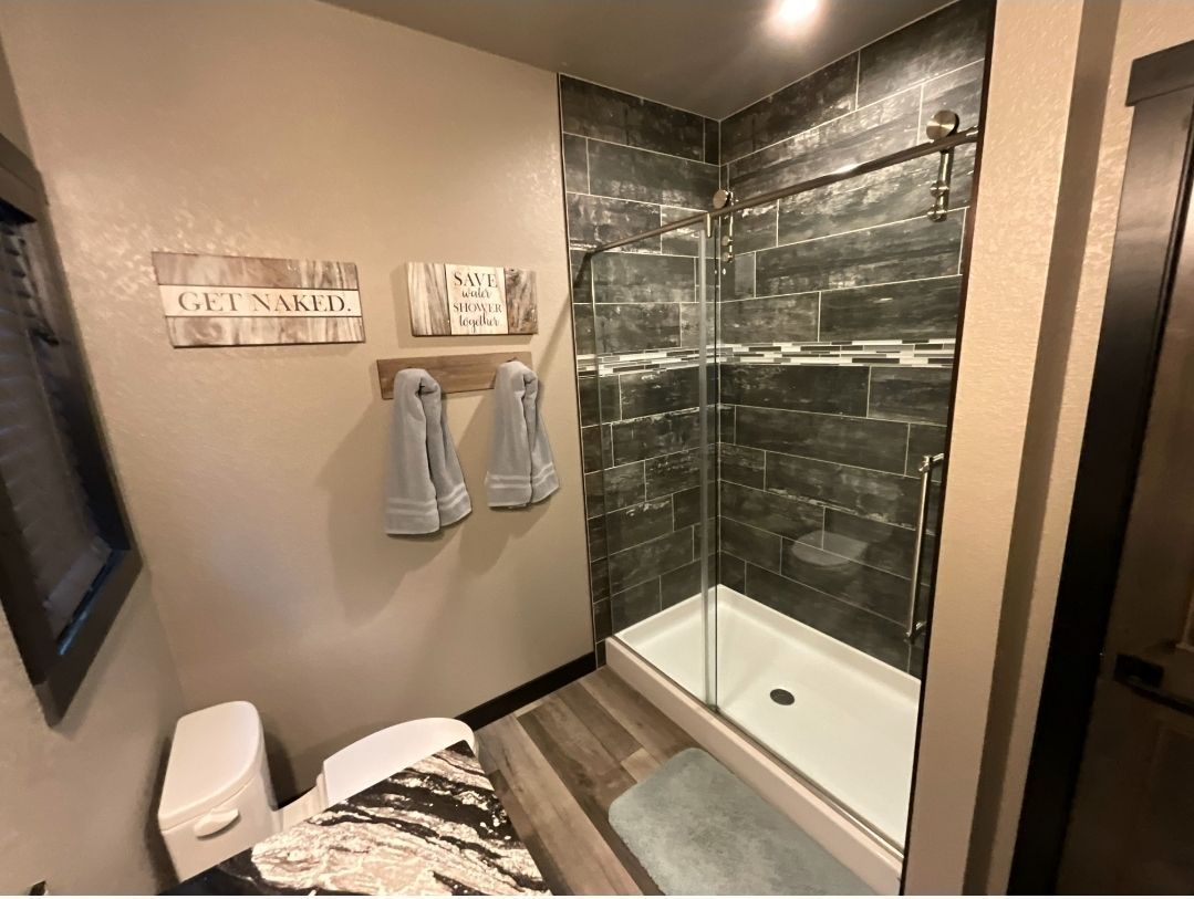 Small bathroom with gray tile shower, toilet, and towels on the wall.