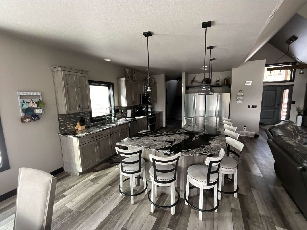 Kitchen with island, cabinets, and bar stools. Gray-toned wood flooring, black countertops, and stainless steel appliances.