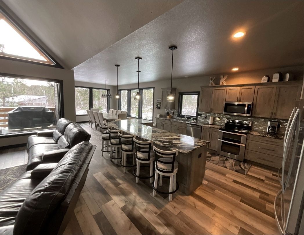 Open-concept kitchen with large island, cabinets, appliances, and seating. View of living room and snowy outdoors.