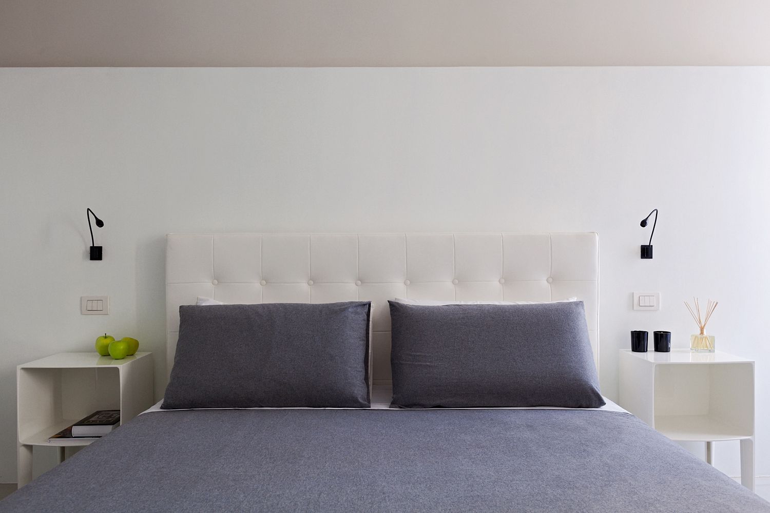 Una cama con cabecero blanco y almohadas grises en un dormitorio.