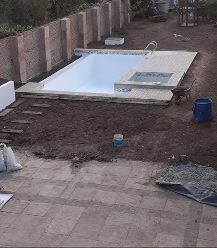 Piscina rectangular de nueva construcción con jacuzzi, ubicada en un patio trasero. Tonos tierra: marrón, beige y blanco.
