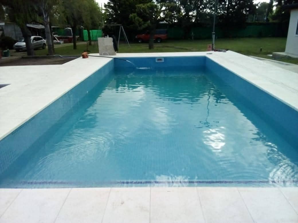 Piscina rectangular de agua azul y borde de azulejos blancos. Exterior, día soleado.