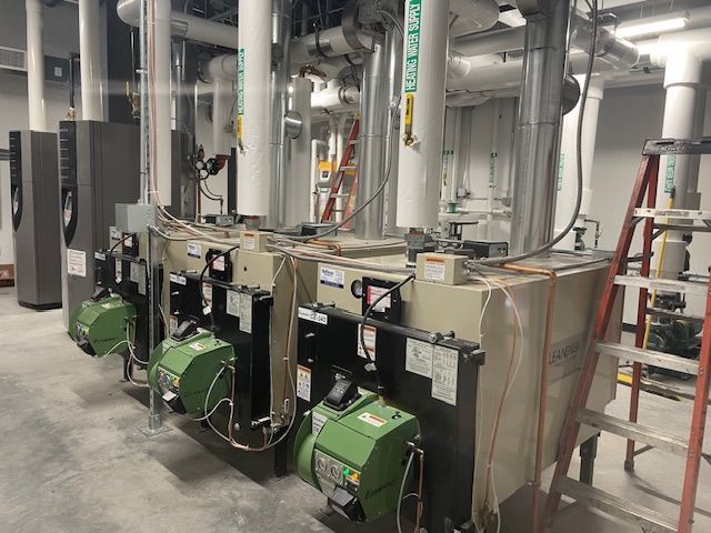 A row of boilers are lined up in a room next to a ladder.