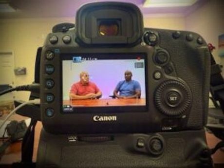 Close-up of a Canon DSLR camera recording two men in an interview setting. Close-up of a Canon DSLR camera recording two men in an interview setting.