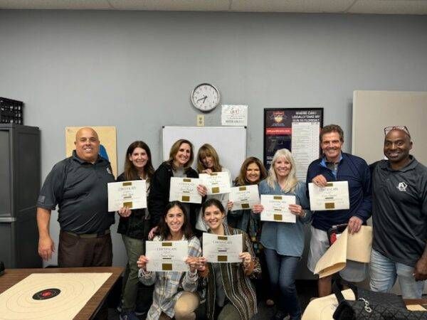 Group of people holding certificates, smiling for the camera. They are indoors in a classroom setting.