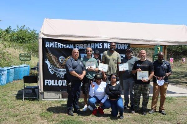 Group of people pose with certificates at an outdoor event under a tent with 