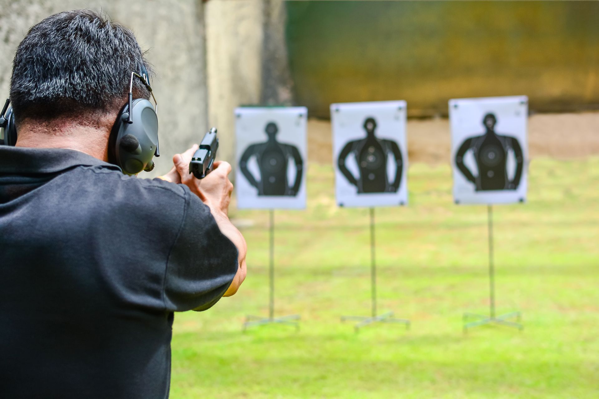 A man at a shooting range aims a handgun at three human-shaped targets.