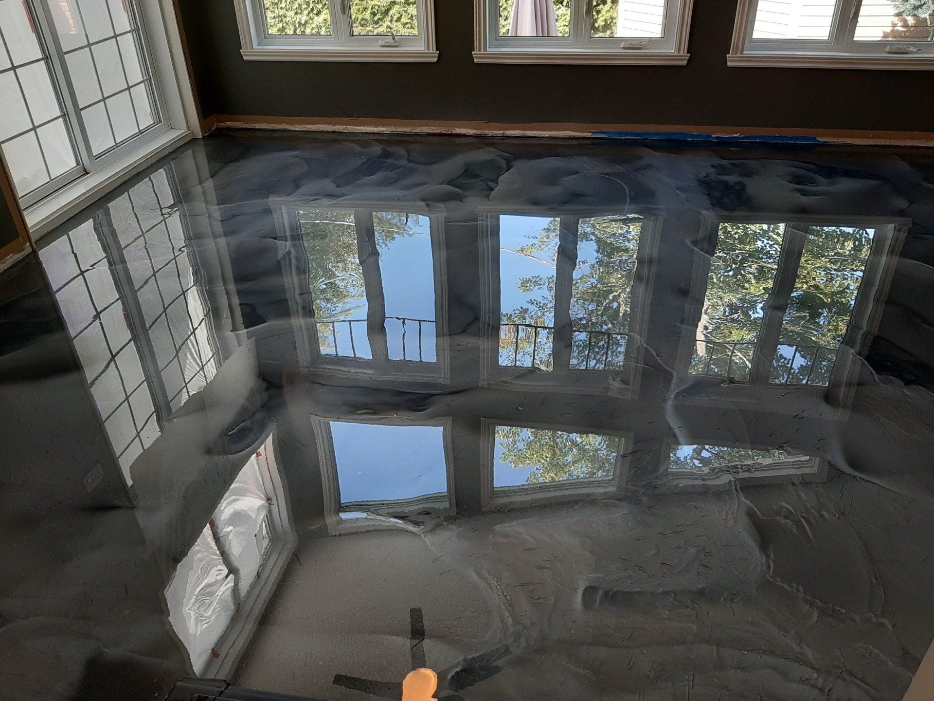 Une pièce avec un ventilateur de plafond et un reflet de fenêtres dans le sol.