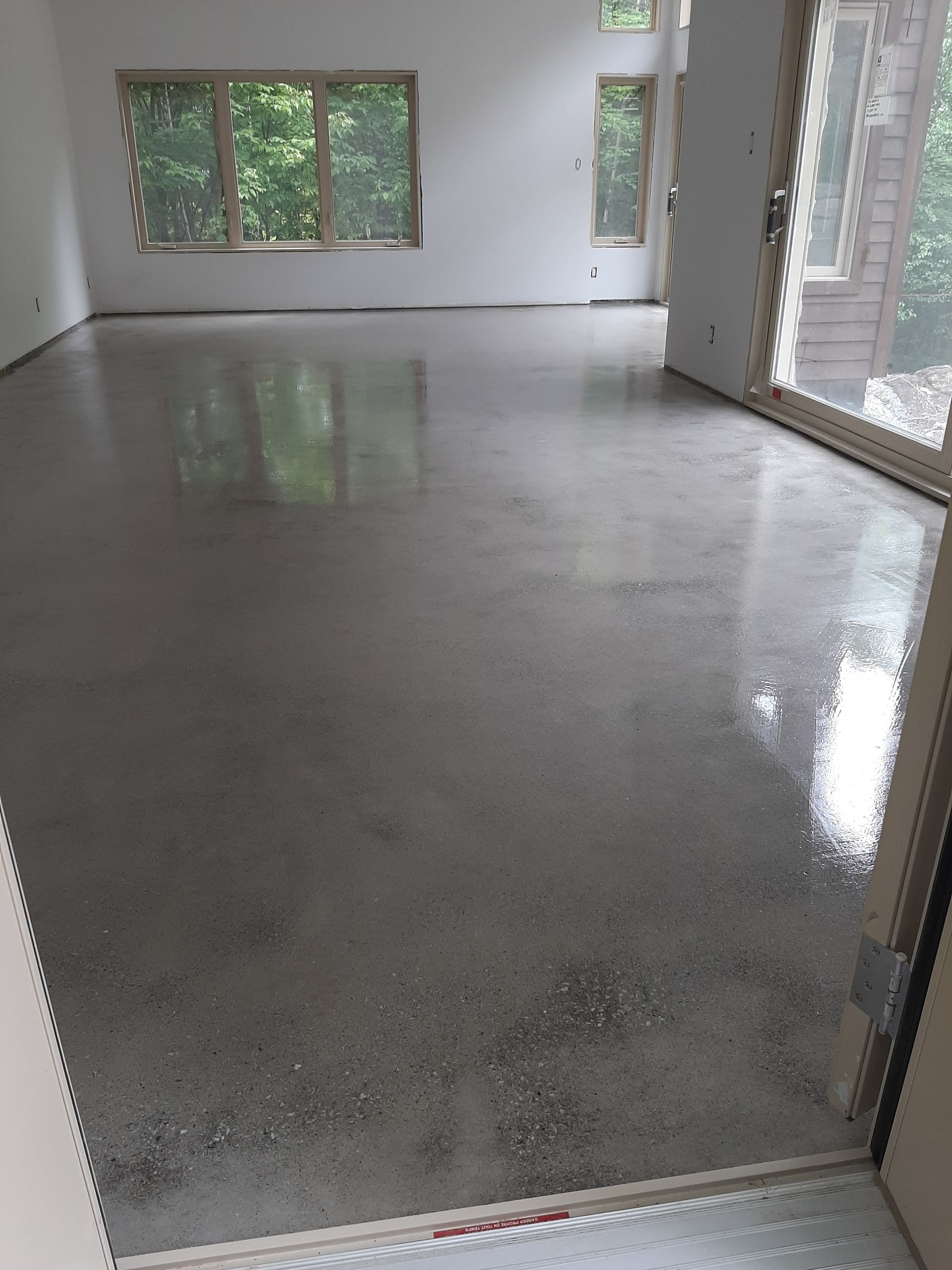 Sol en béton poli dans une pièce vide, reflétant la lumière des fenêtres et d'une porte vitrée.
