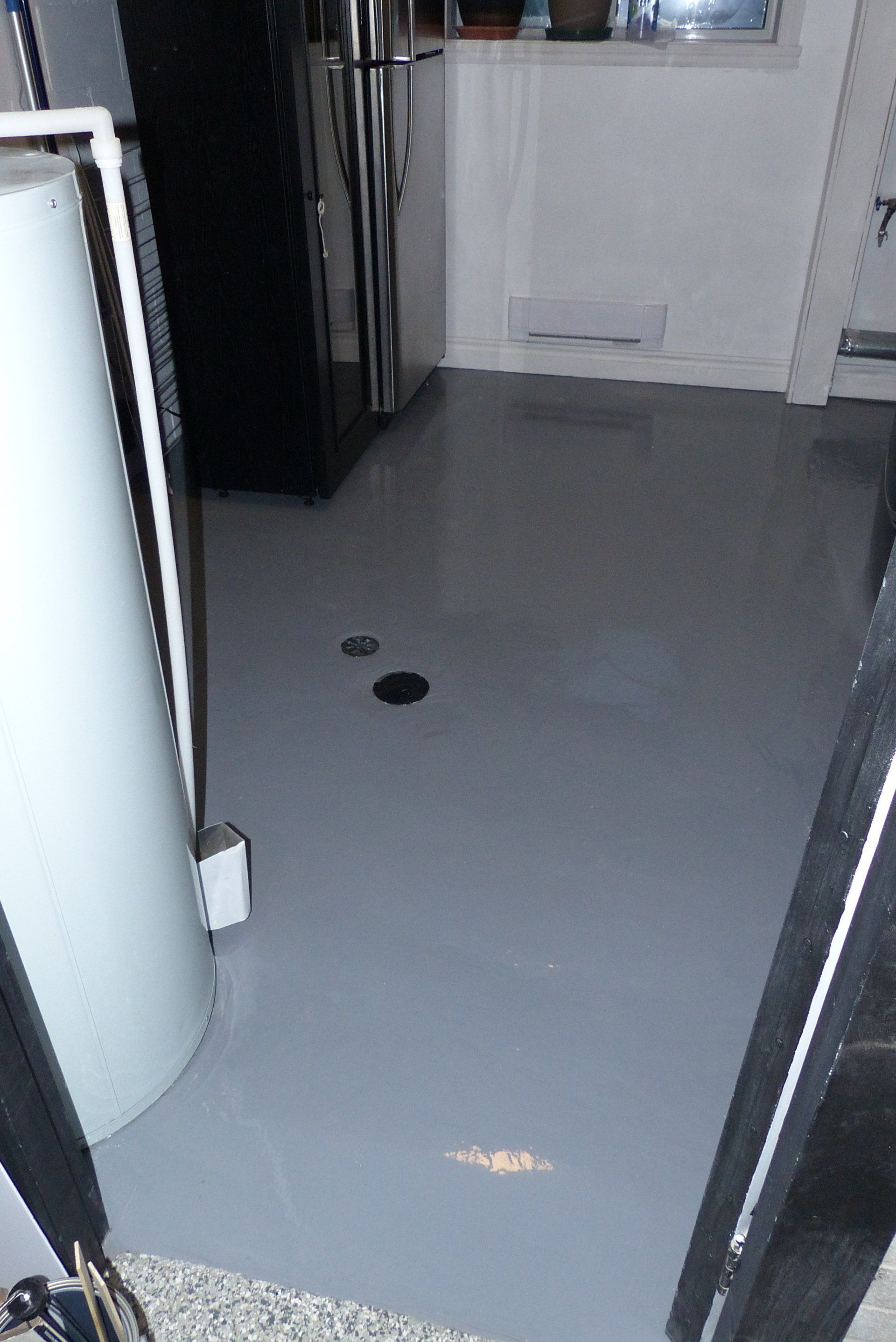 Une cuisine avec un sol gris et un réfrigérateur noir.