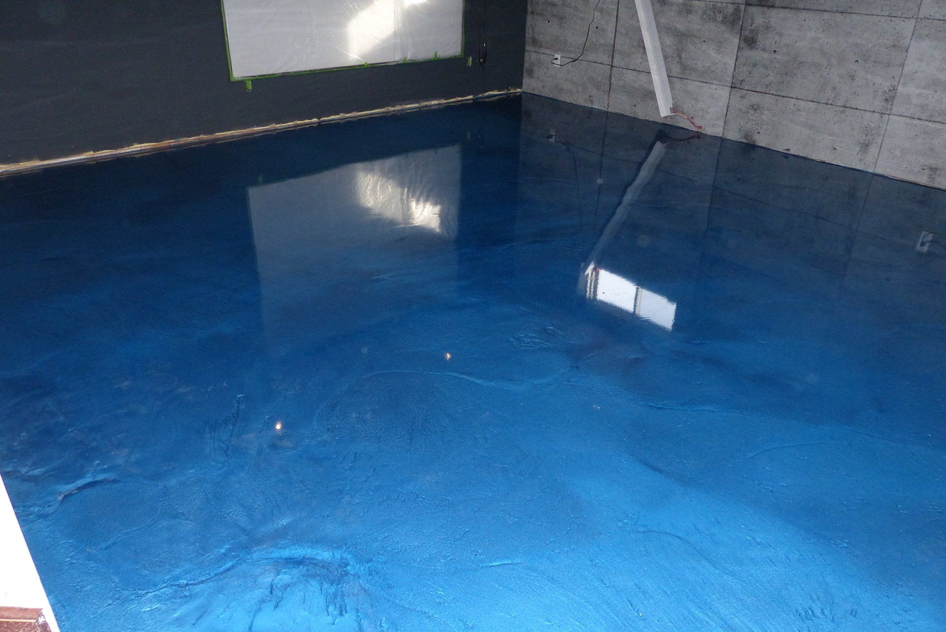 Un sol métallique bleu dans une pièce avec le reflet d'une fenêtre.