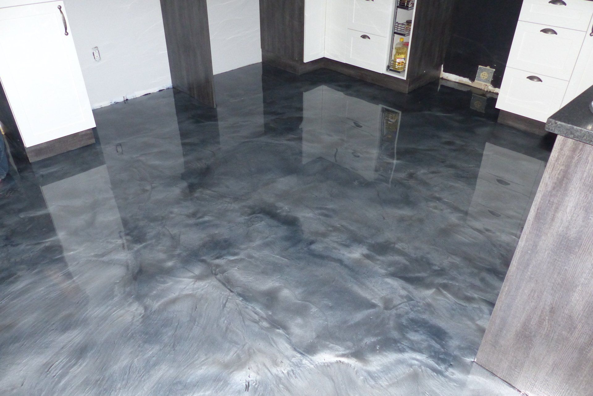 Une cuisine avec un sol métallique noir et des armoires blanches.