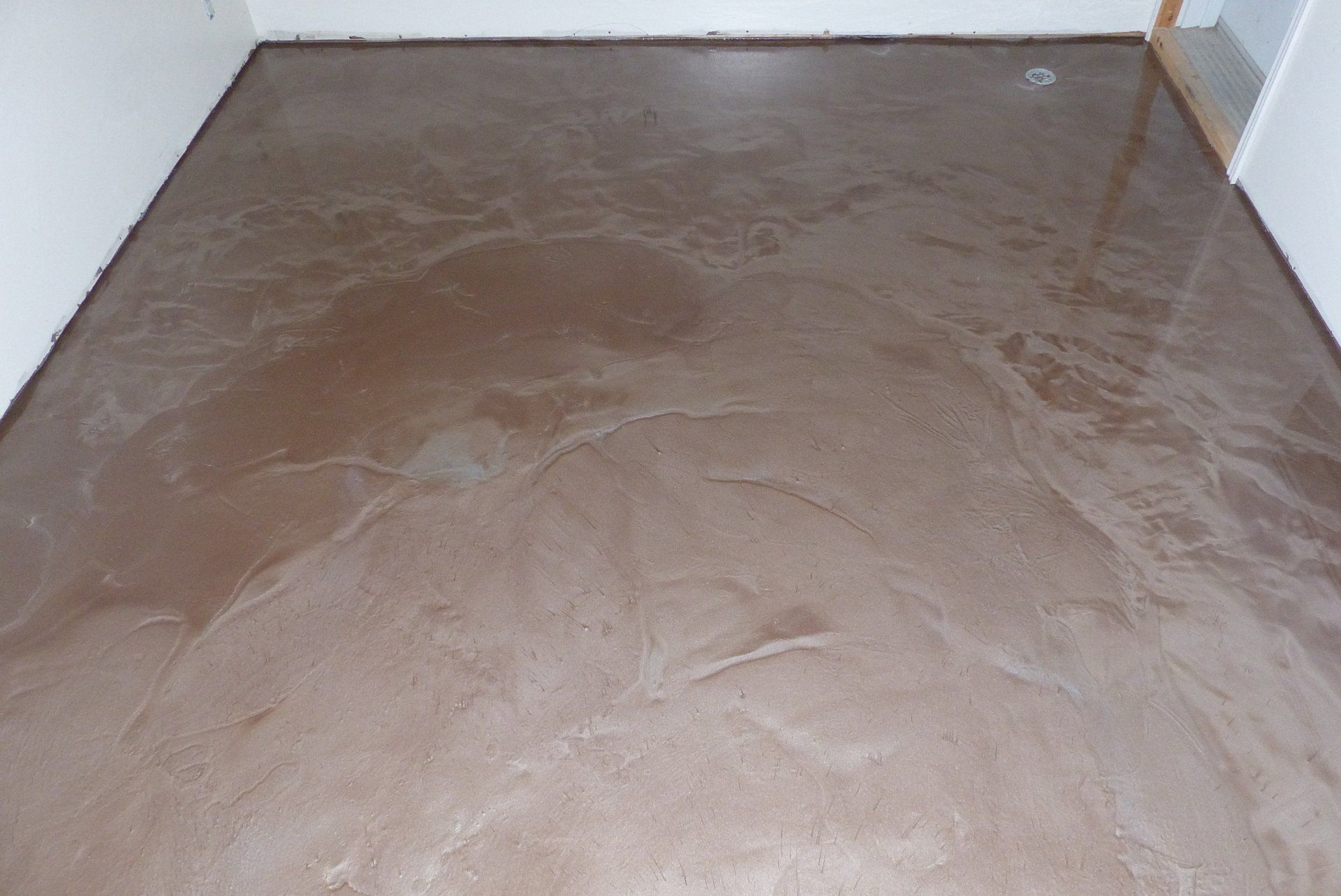 Un sol en béton marron dans une pièce avec un mur blanc.