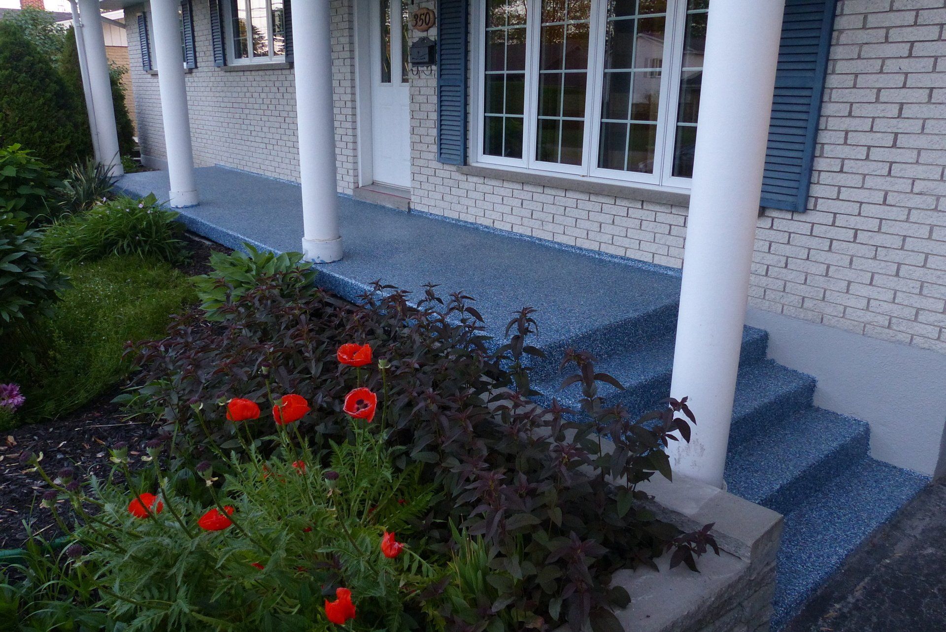 Une maison en briques blanches avec des marches bleues et des fleurs devant