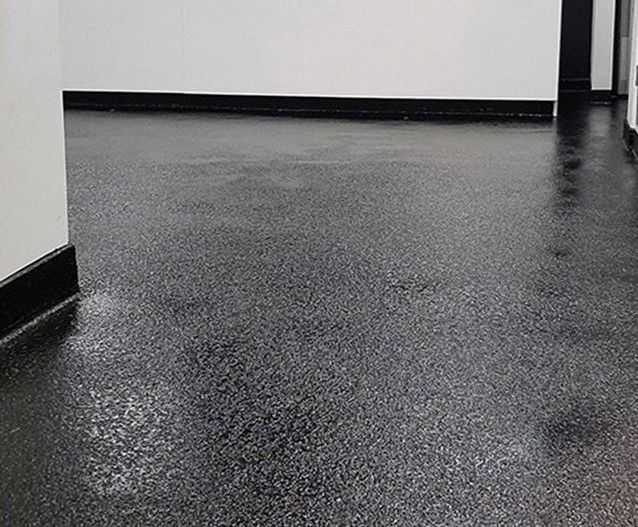 Un couloir avec un sol noir et des murs blancs.