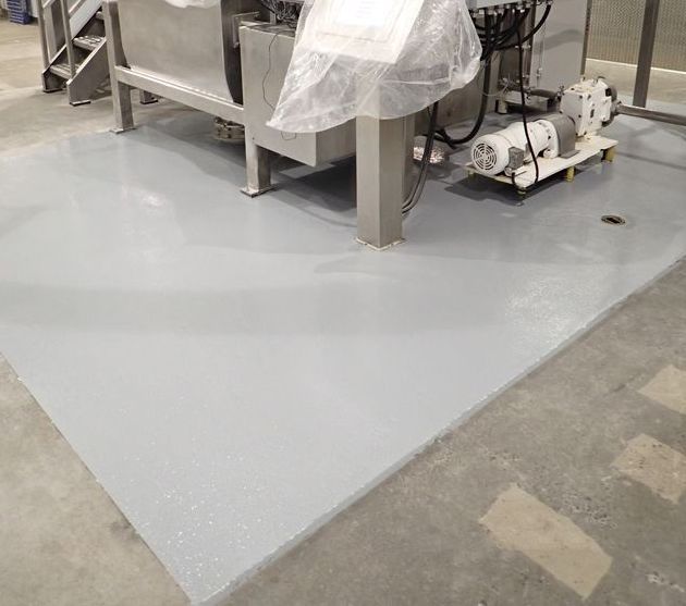 Revêtement de sol industriel gris autour d'une machine dans un environnement d'usine.